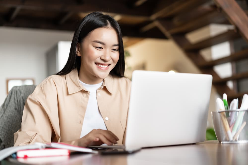 smiling-asian-girl-waching-webinar-having-work-video-call-from-home-working-freelance-remotely-looki